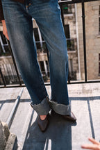 Nahaufnahme einer blauen Jeans mit breitem Fransenumschlag und spitzen braunen Schuhen.