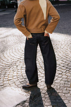Rückansicht einer Frau in kamelfarbener Jacke und dunkelblauer Wide-Leg-Jeans auf Kopfsteinpflaster.