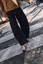 Frau in kamelfarbener Jacke und dunkelblauer Wide-Leg-Jeans beim Überqueren eines Zebrastreifens.