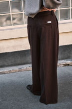 Rückansicht einer dunkelbraunen Wide-Leg-Hose mit weißem Logo-Label an der Gesäßtasche und grauem Pullover.