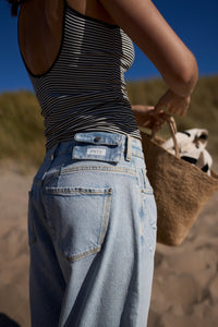 Detailansicht: Frau trägt Hose am Strand, der Fokus liegt auf einer kleinen Tasche, die hinten am Bund befestigt ist.