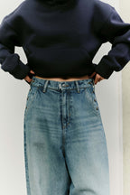 Nahaufnahme des Hosenbunds einer weit geschnittenen Jeans mit dekorativen Knopfdetails an den Taschen und dunkelblauem Hoodie.