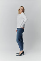 Frau in weißem Langarmshirt und blauer Jeans mit Fransensaum in der Seitenansicht.