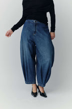 Vorderansicht einer weiten blauen Ballon-Jeans mit markanten Falten am Saum und schwarzen Pumps.