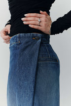 Detailaufnahme einer blauen Jeans mit markantem Wickel-Verschluss und einem Knopf am Bund.
