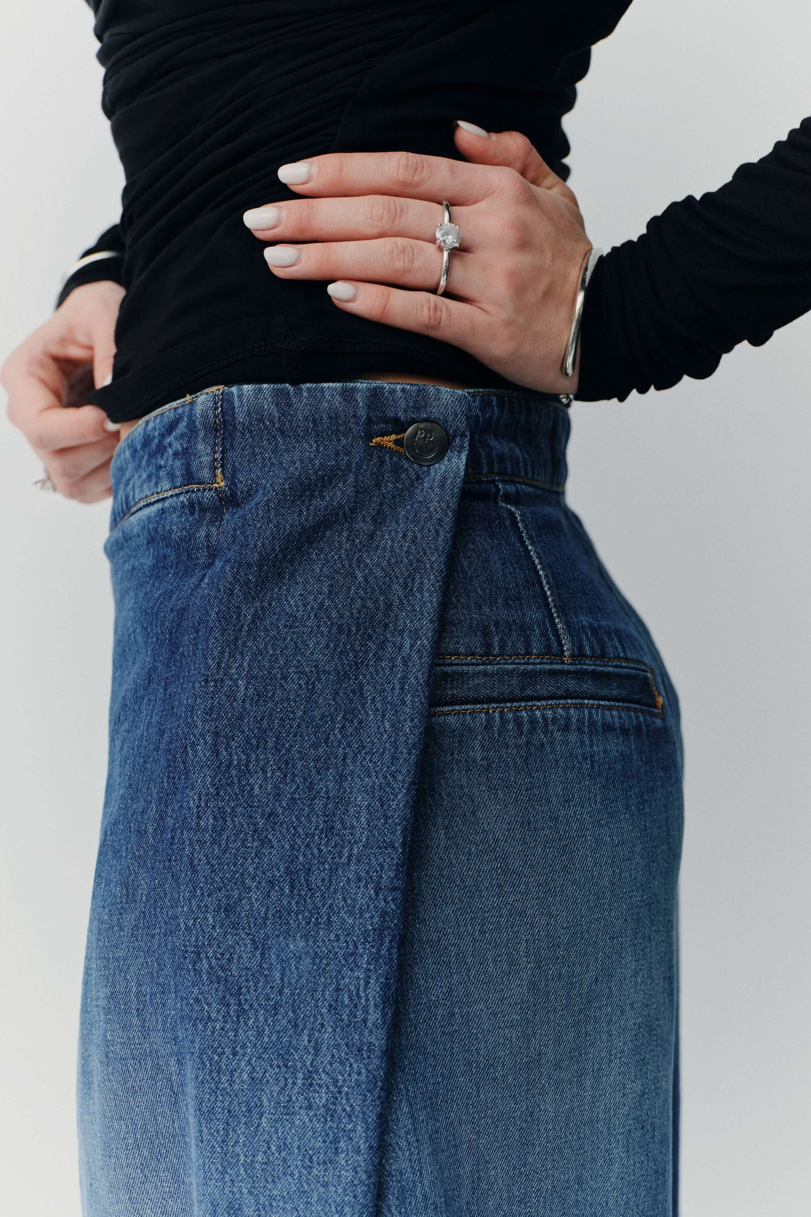 Detailaufnahme einer blauen Jeans mit markantem Wickel-Verschluss und einem Knopf am Bund.