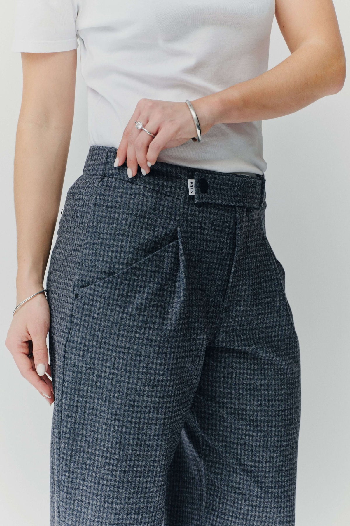 Detailansicht einer grau-blau gemusterten Hose mit feinem Muster und Logo-Detail am Bund.