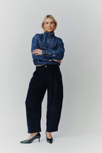 Frau in einem dunkelblauen Denim-Troyer und einer weiten dunkelblauen Cordhose vor hellem Hintergrund.