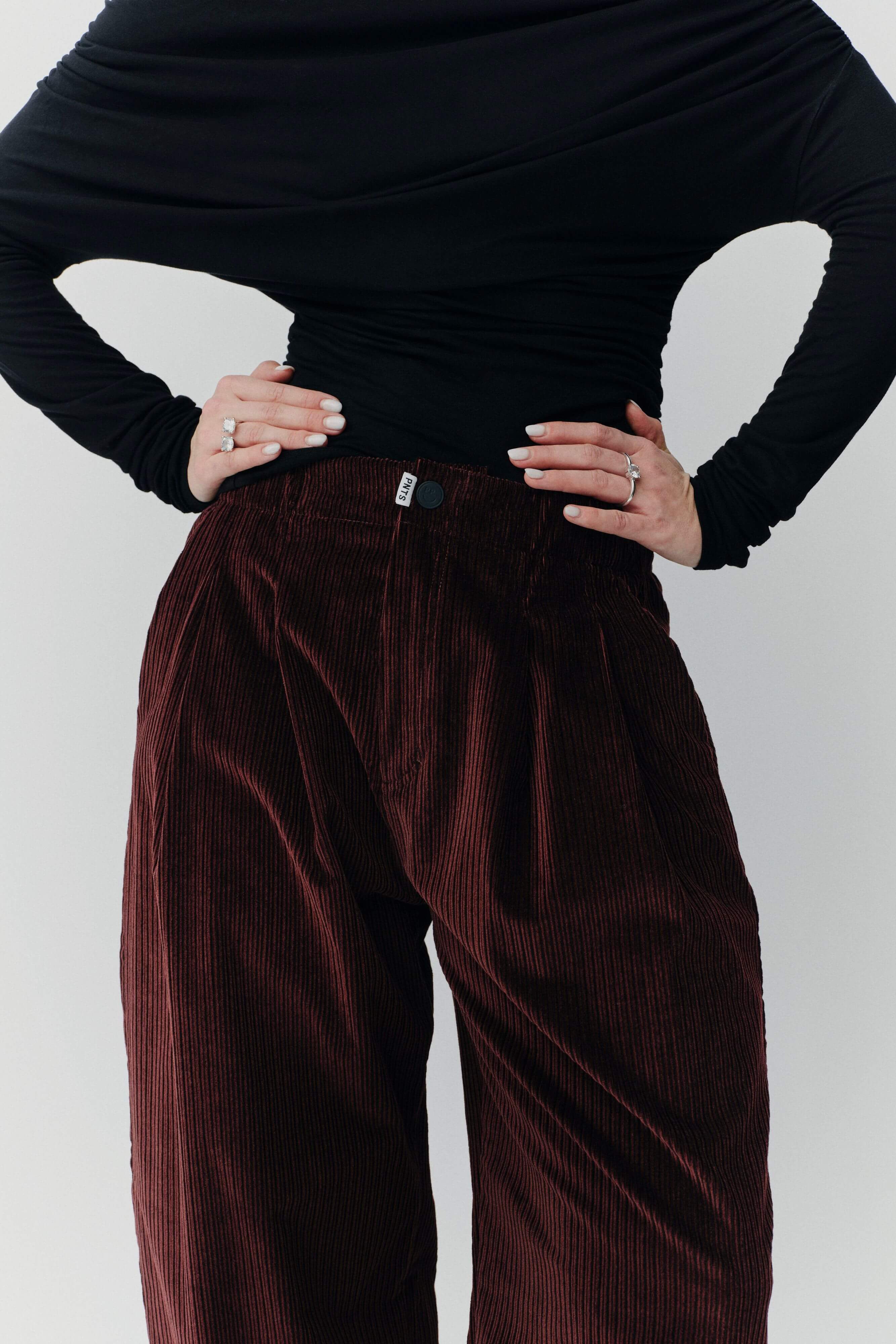 Detailaufnahme einer dunkelroten Cordhose mit weitem Bein und einem schwarzen, langärmeligen Oberteil.
