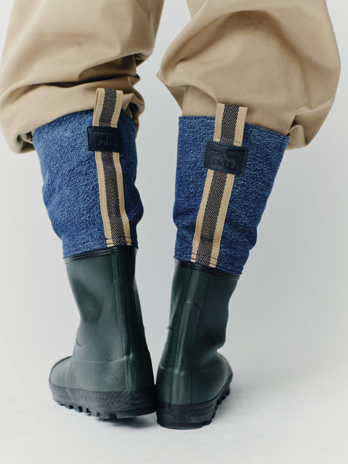 Rückansicht-Detail: Dunkelgrüne Outdoor-Gummistiefel mit blauem Textilschaft, gestreifter Zuglasche und geprägtem PNTS-Logo-Patch.