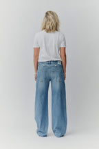 Rückansicht einer Frau in einem weißen T-Shirt und einer weiten blauen Jeans mit PNTS-Label am Bund.