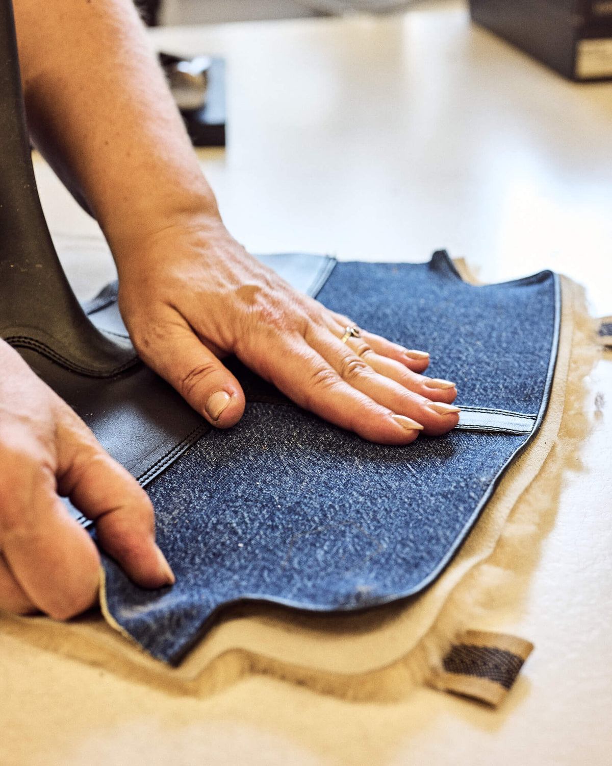 Handwerkliche Schuhfertigung: Hände legen das blaue Denim-Obermaterial mit weichem Lammfell-Innenfutter passgenau für den Stiefelschaft zusammen.