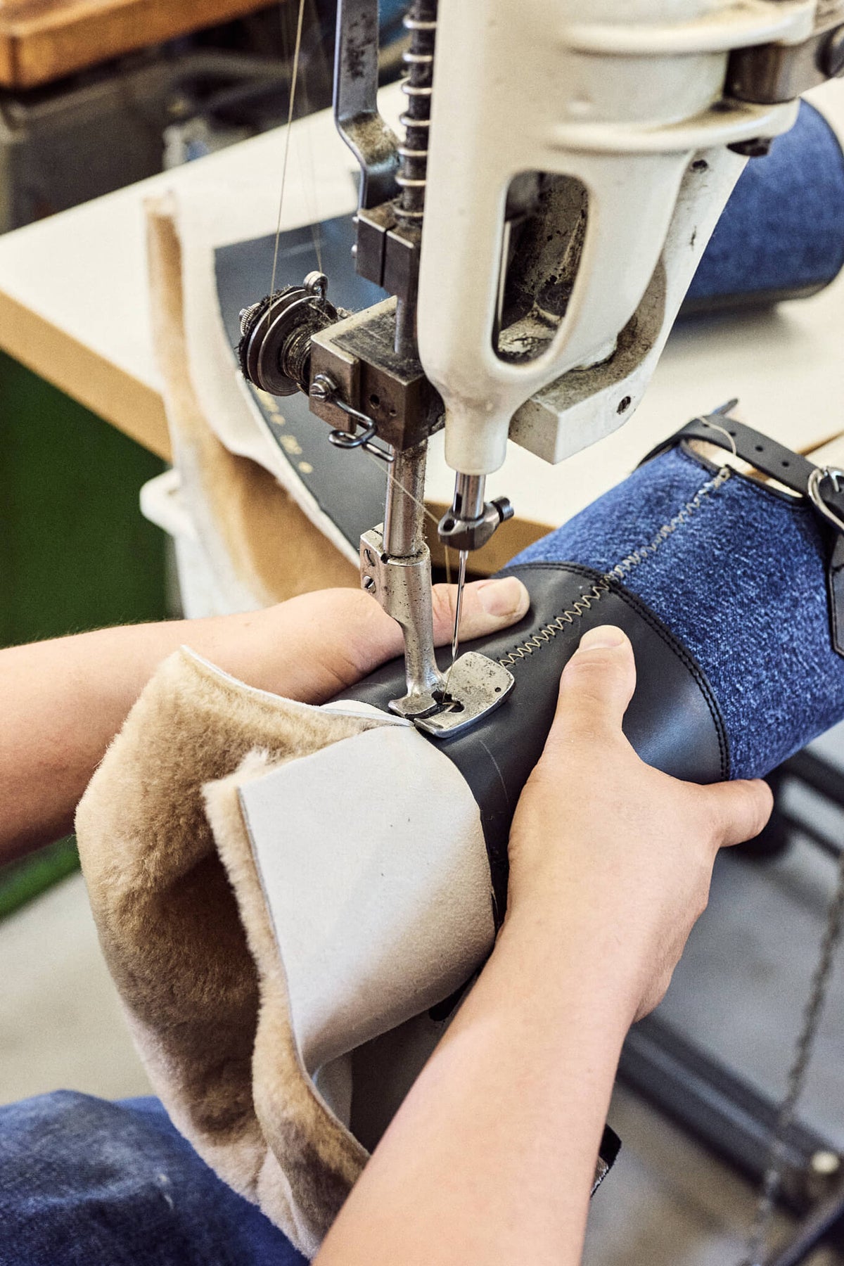 Traditionelles Schuhmacherhandwerk: Der Stiefelschaft aus Leder, blauem Textil und wärmendem Lammfellfutter wird an einer Industrie-Nähmaschine zusammengenäht.