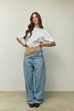 Frau in weißem T-Shirt und weiter hellblauer Jeans mit einem beigen Paisley-Bandana als Gürtel-Detail.