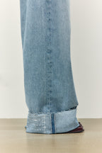 Nahaufnahme eines hellblauen Jeansbeins mit breitem Umschlag und weißer Hilfsnaht als Markierung zum Kürzen.