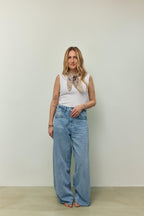 Frau in weißem ärmellosem Top und weiter hellblauer Jeans, kombiniert mit einem beigen Paisley-Bandana als Halstuch.
