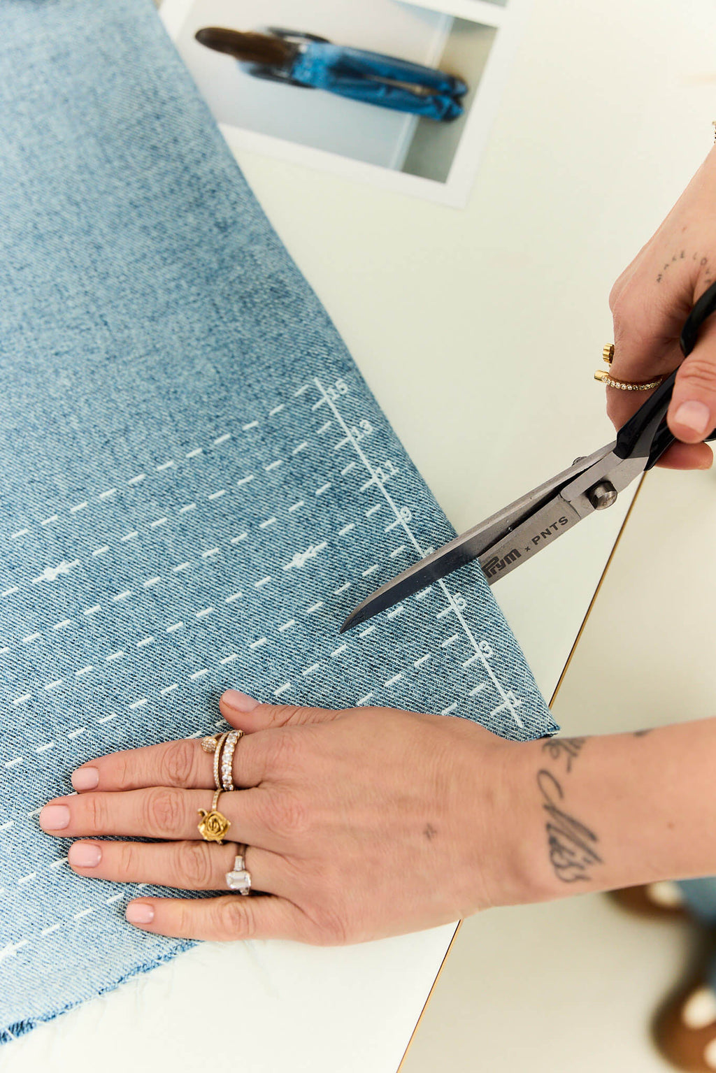 Nahaufnahme: Hände schneiden einen Denim-Stoff mit einer Schere entlang einer aufgedruckten weißen Skala zu.