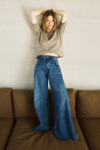Eine Frau steht auf einem Sofa und ist leicht an eine Wand gelehnt. Sie trägt eine Jeans mit einem weiten Bein 32_THE HIP HOP in dunkelblau.