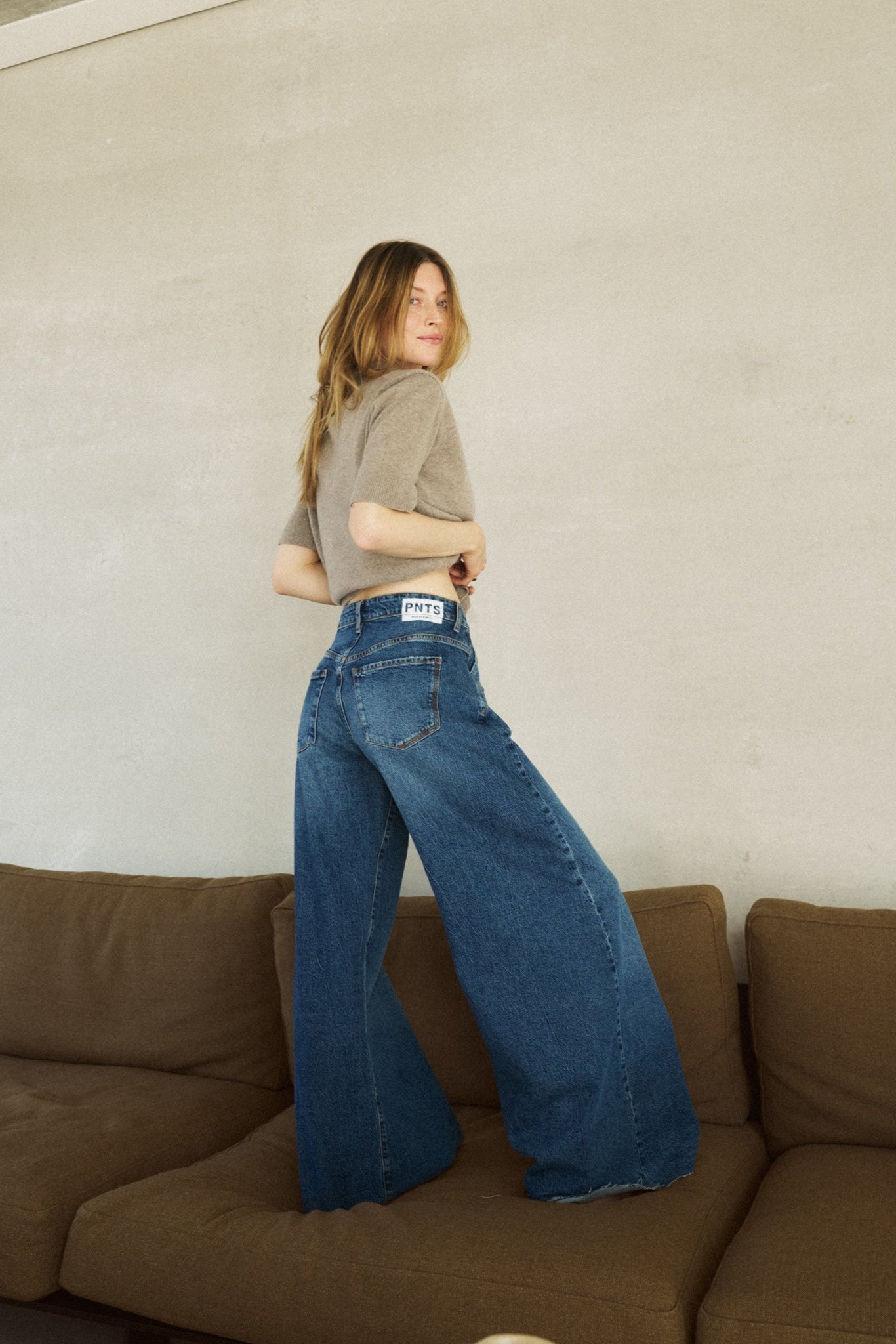 Eine Frau steht auf einem Sofa. Man sieht die Jeans von hinten, mit einem sehr weiten Bein 32_THE HIP HOP in dunkelblau.
