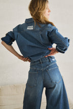 Man sieht eine Frau von hinten. Sie trägt ein Jeanshemd mit weißen Streifen 27_THE SUIT UP BLOUSE STRIPES in mittelblau und die passenden Jeans mit weißen Streifen 05_THE O SHAPE EXTREME STRIPES in mittelblau.