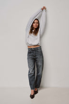 Frau in hellgrauem Sweatshirt und dunkelgrau gewaschener Jeans vor weißem Hintergrund.