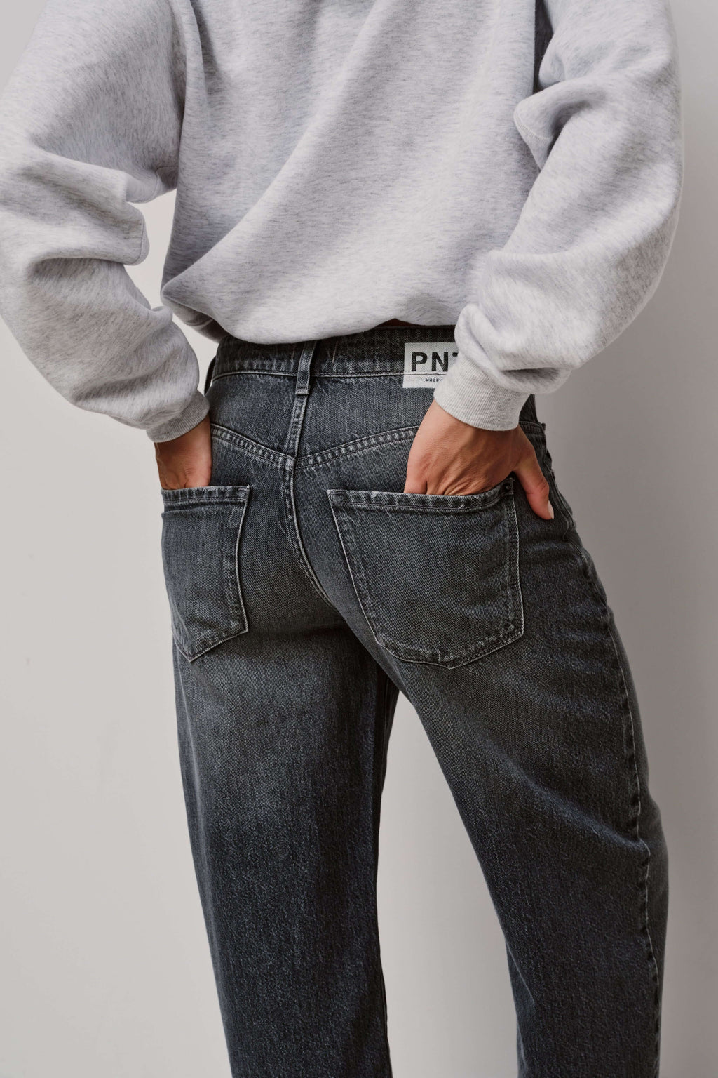 Detailaufnahme der Rückansicht einer dunkelgrau gewaschenen Jeans mit Logo-Patch am Bund.