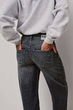 Detailaufnahme der Rückansicht einer dunkelgrau gewaschenen Jeans mit Logo-Patch am Bund.