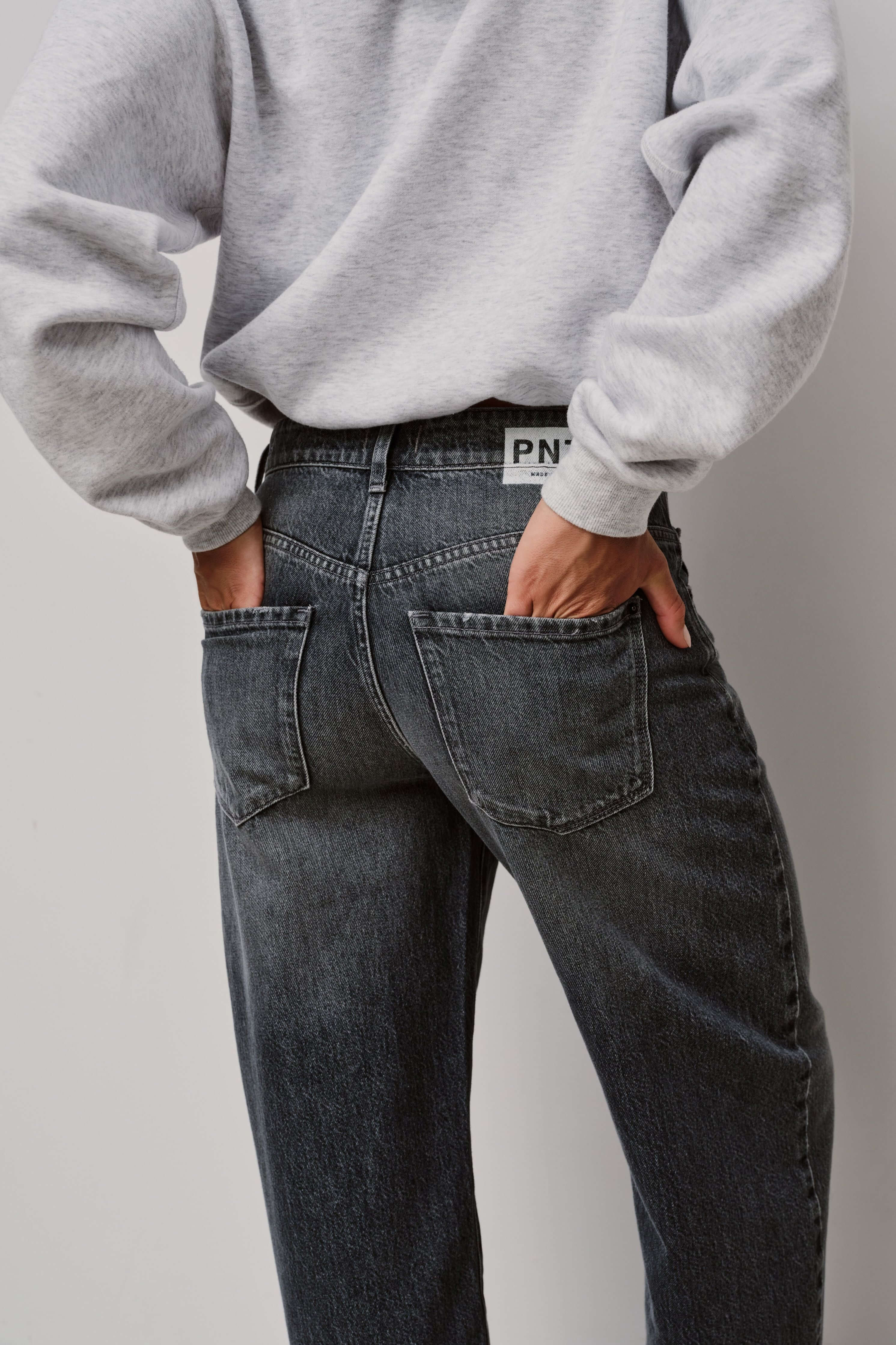 Detailaufnahme der Rückansicht einer dunkelgrau gewaschenen Jeans mit Logo-Patch am Bund.