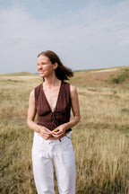 Frau in strukturiertem braunem Bindetop und weißer Hose in einer weiten Graslandschaft.