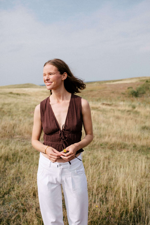 Frau in strukturiertem braunem Bindetop und weißer Hose in einer weiten Graslandschaft.