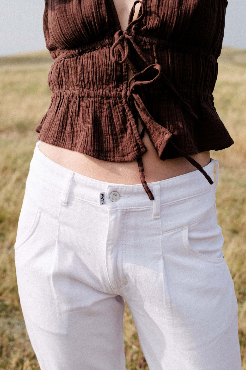 Nahaufnahme eines strukturierten braunen Bindetops kombiniert mit einer weißen Hose mit PNTS-Label am Bund.