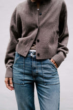 Braune Strickjacke kombiniert mit blauer Jeans und markanten, aufgesetzten Fronttaschen.