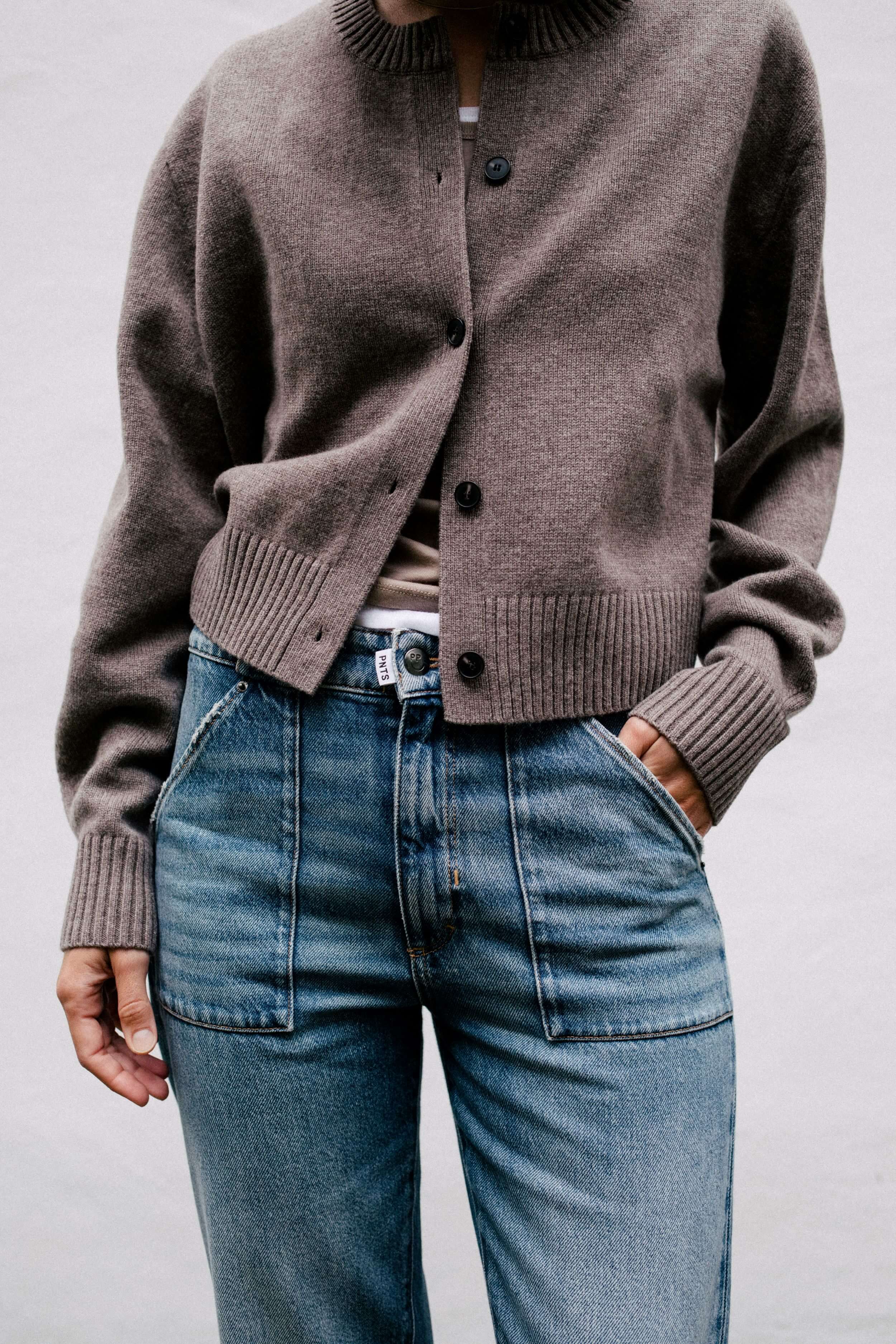 Braune Strickjacke kombiniert mit blauer Jeans und markanten, aufgesetzten Fronttaschen.
