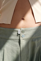 Detailansicht einer grünen Leinenhose mit zwei Knöpfen auf denen der PNTS Smiley zu sehen ist. Zudem hat die Hose ein PNTS Fähnchen.