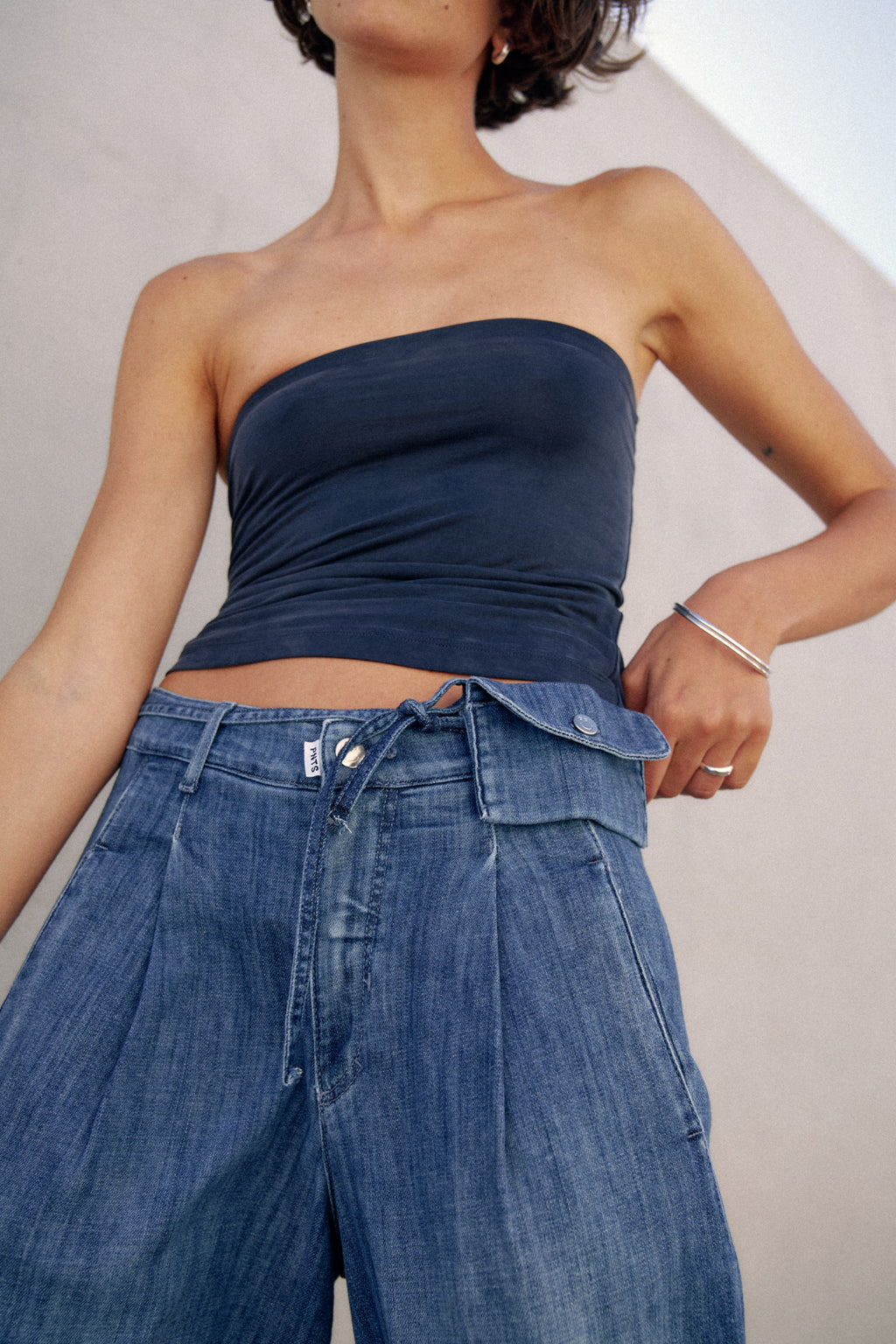 Detailansicht einer Jeanshose. Die Hose hat ein Jeansband mit einer kleinen Tasche als Gürtel.