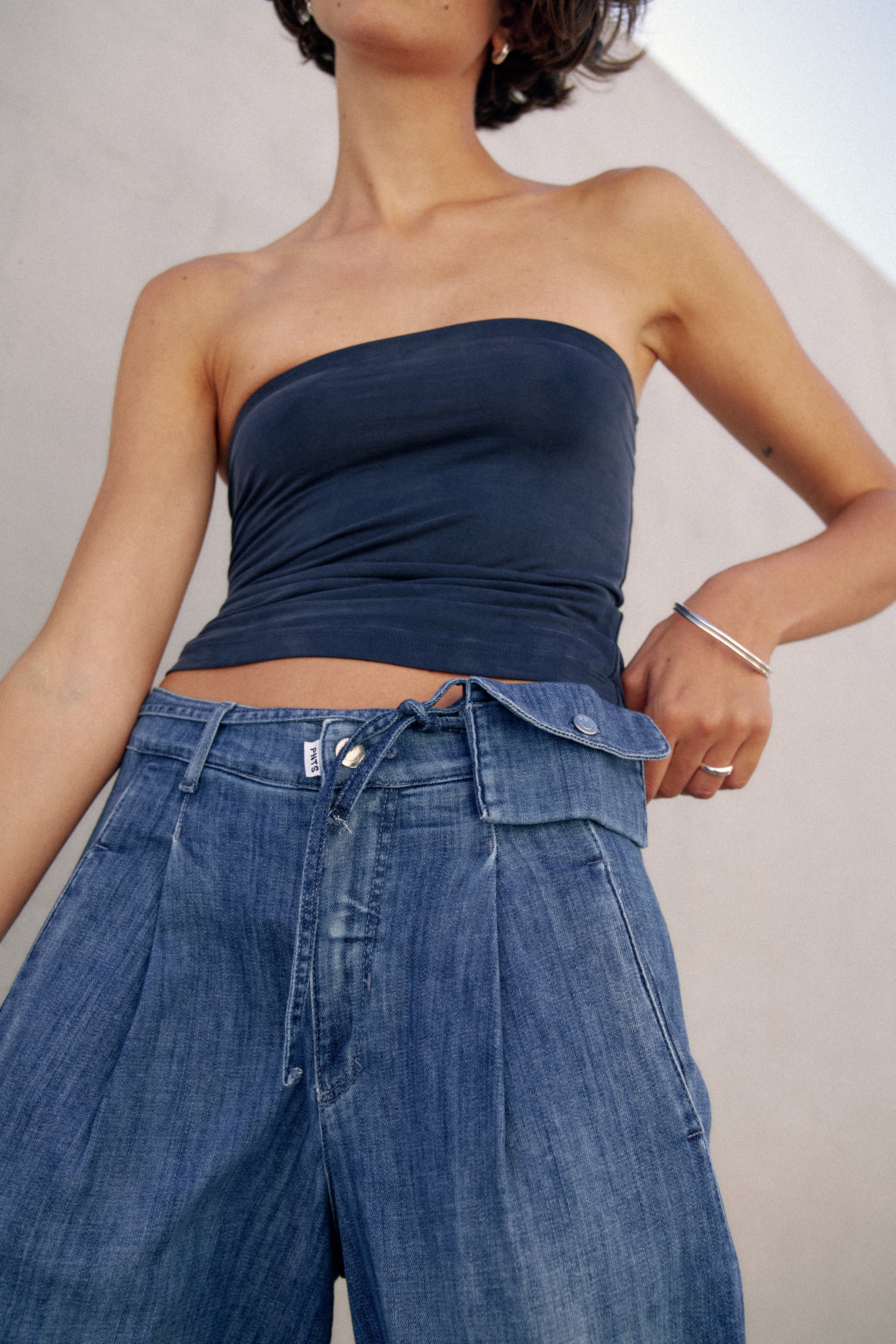 Detailansicht einer Jeanshose. Die Hose hat ein Jeansband mit einer kleinen Tasche als Gürtel.