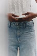 Ein Detailfoto von einer hellen Jeans. Sichtbar ist der PNTS Knopf und das Fähnchen an der Hose. 