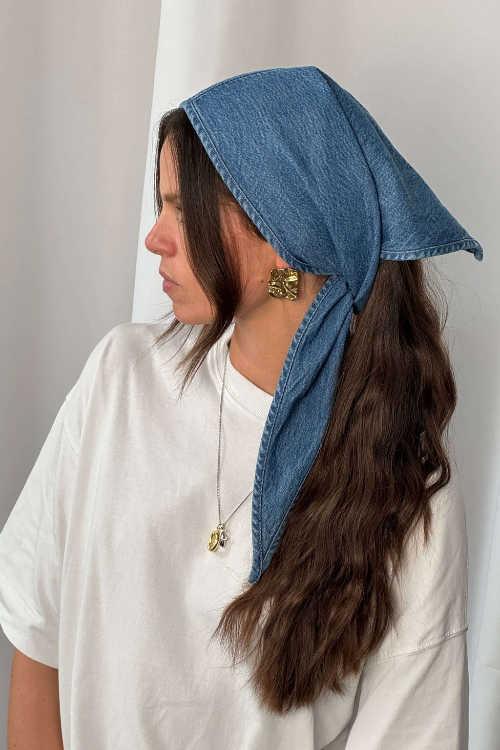 Frau in weißem Oversized-T-Shirt trägt ein blaues Denim-Bandana als Kopftuch.